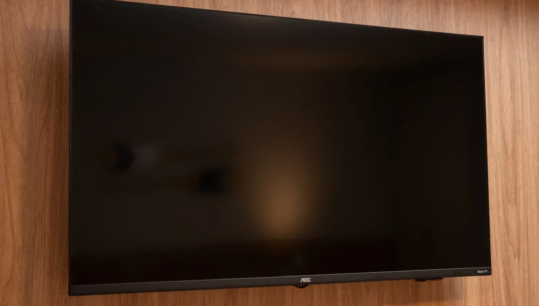 Televisor AOC de tela plana montado na parede da pousada, oferecendo entretenimento para os hóspedes com canais e recursos modernos.