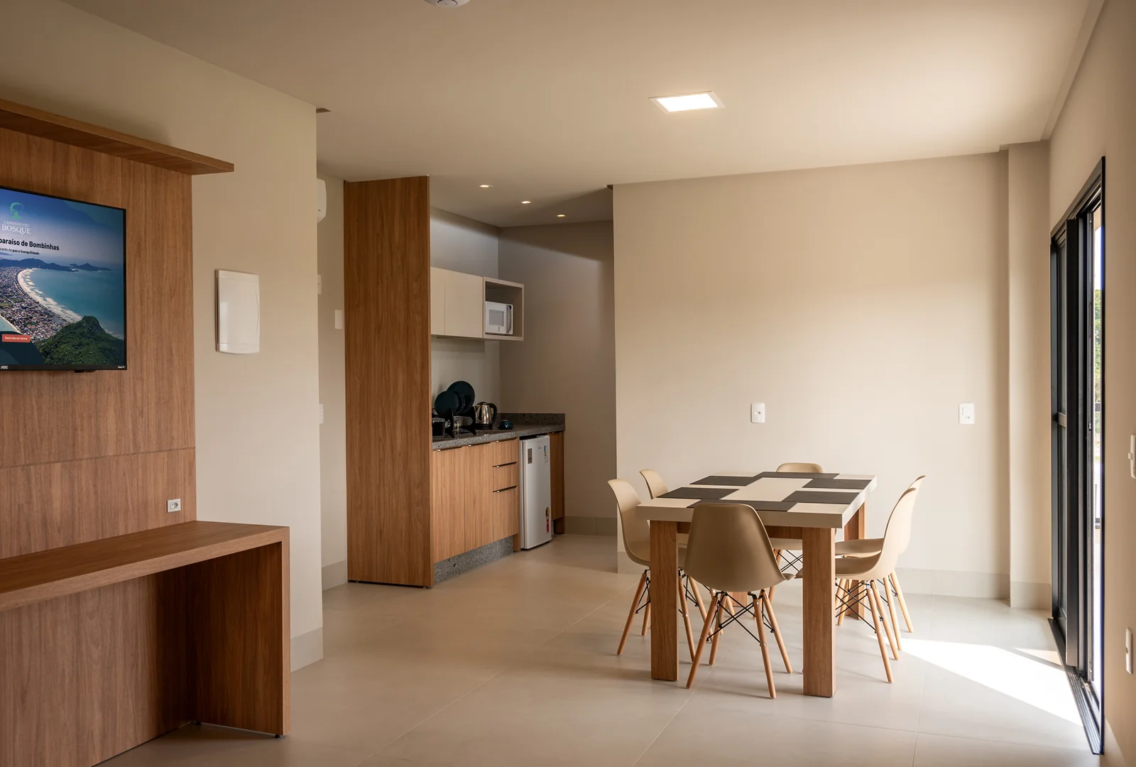 Sala de estar espaçosa com mesa de jantar e cozinha equipada, ideal para refeições em família na unidade  da Pousada Caminho do Bosque.