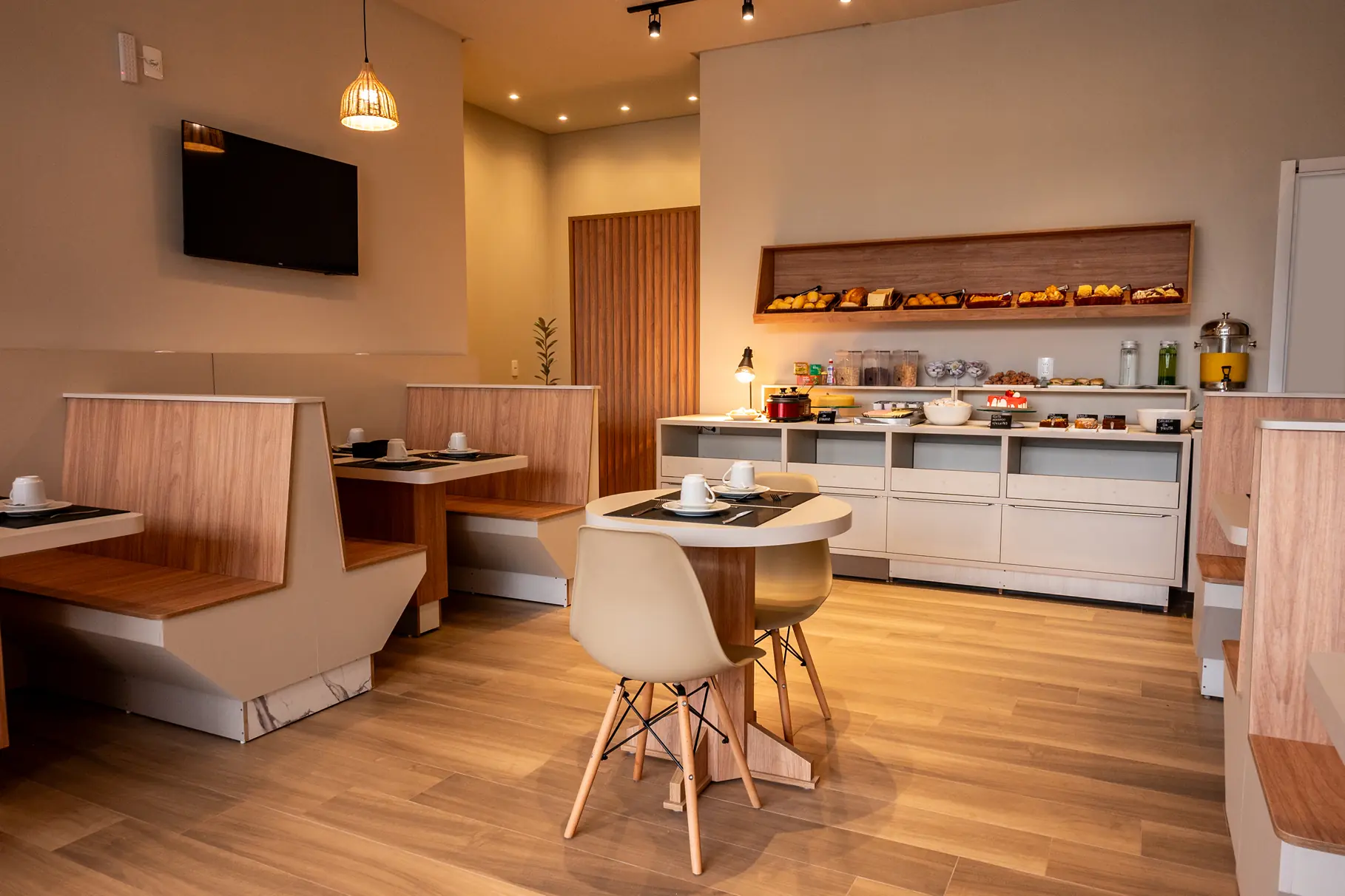 Salão de café da manhã da Pousada Caminho do Bosque, com ambientes modernos, decoração elegante em madeira clara e buffet variado com opções deliciosas para começar bem o dia.