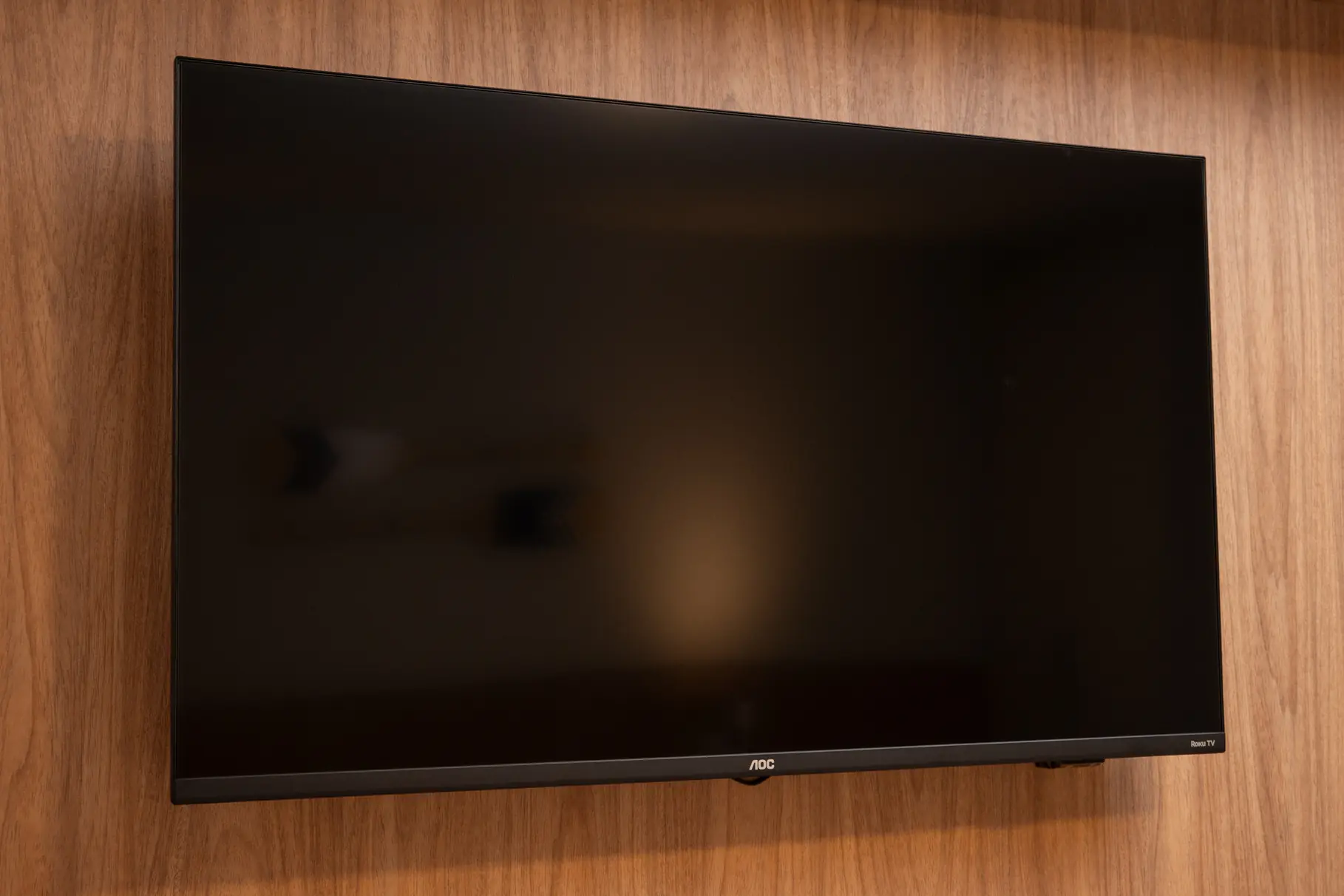 Televisor AOC de tela plana montado na parede da pousada, oferecendo entretenimento para os hóspedes com canais e recursos modernos.