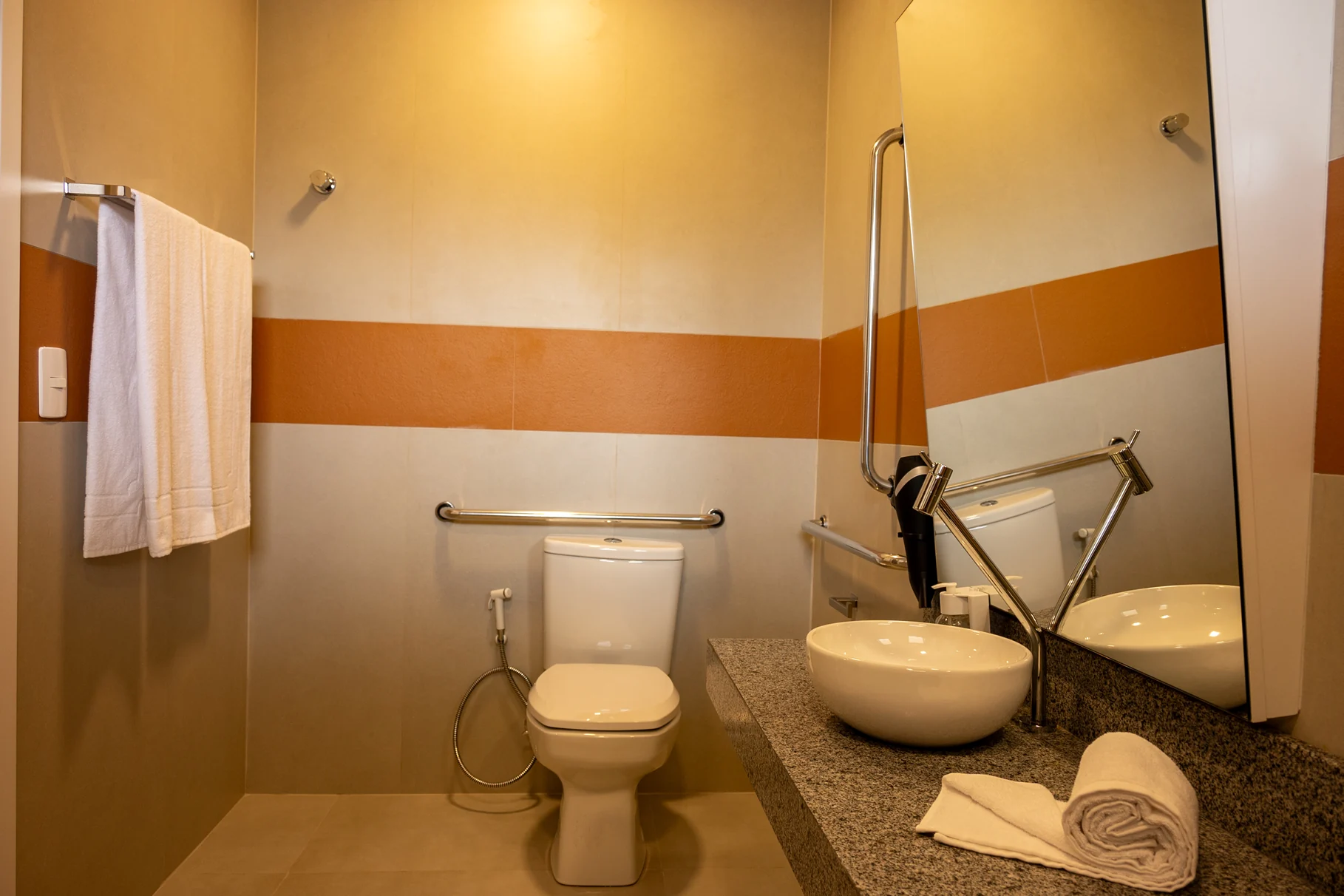 Banheiro adaptado da pousada, equipado com barras de apoio, espelho inclinado e pia com design moderno. Ideal para hóspedes que buscam conforto e acessibilidade em sua estada.