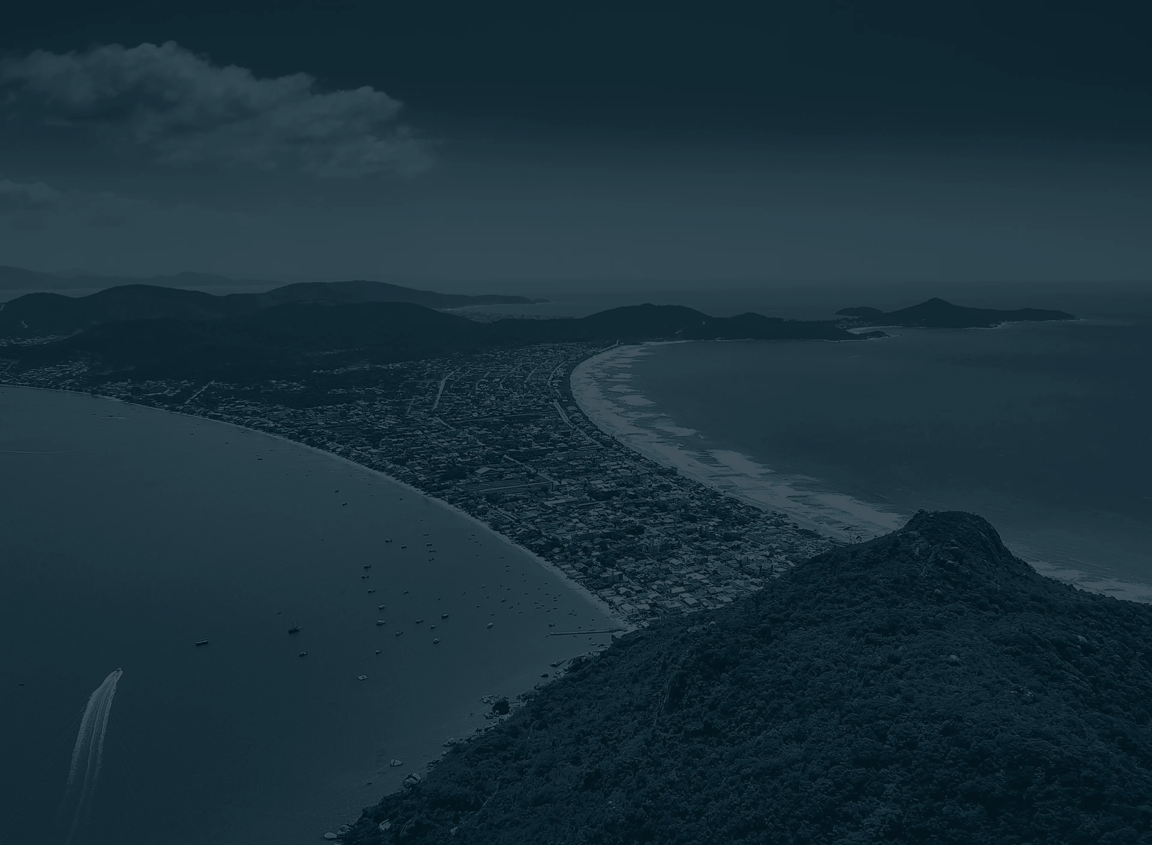 Vista aérea de Bombinhas, Santa Catarina, mostrando a praia de Canto Grande e a região montanhosa ao redor, com águas azuis e vegetação exuberante ao fundo.