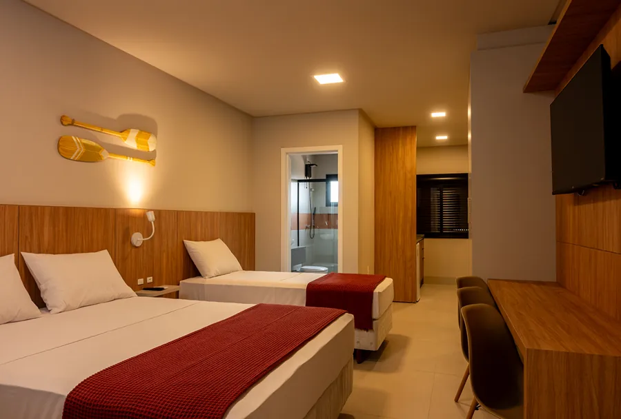 Quarto confortável da Pousada Caminho do Bosque, com decoração aconchegante em tons de madeira, camas de solteiro com roupas de cama impecáveis e banheiro privativo, ideal para uma estada relaxante.